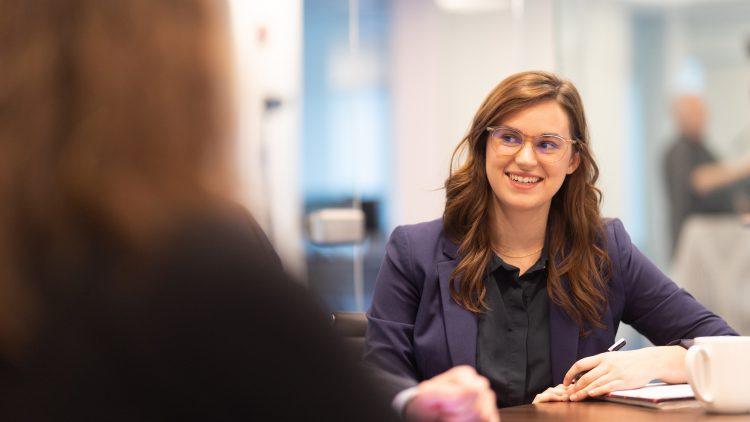 A woman sits in a conference room and chats with a colleague